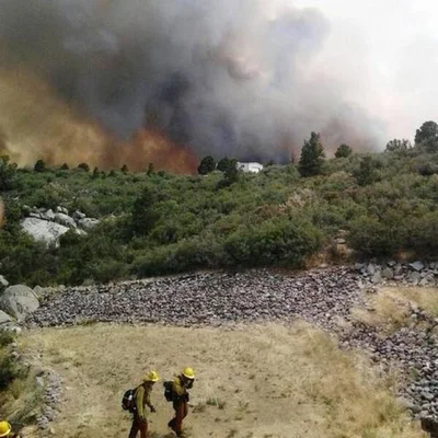 Pompiers avançant près d'un incendie de forêt massif en Arizona, avec une épaisse fumée noire s'élevant derrière eux.