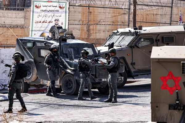 Forces de sécurité israéliennes lors d'un raid en Cisjordanie, avec une affiche à l'effigie d'un Palestinien en arrière-plan.