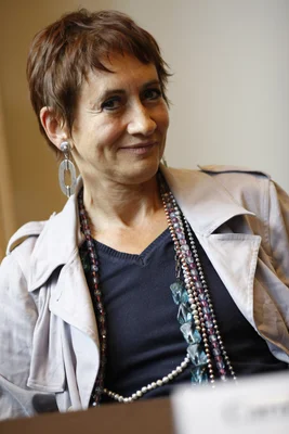 Caroline Loeb, souriante, dans un trench beige et colliers de perles.