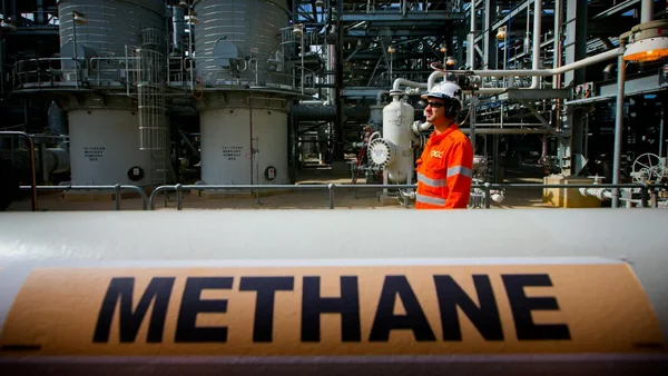 Ouvrier dans une installation industrielle avec une étiquette 'METHANE' sur un tuyau.