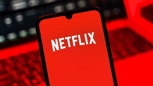 Écran de smartphone montrant le logo Netflix sur fond rouge, avec un clavier d'ordinateur en arrière-plan.