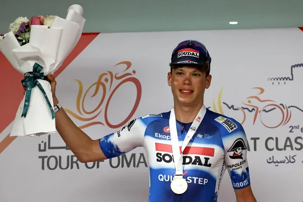 Paul Magnier sur le podium du Tour d'Oman, tenant un bouquet de fleurs.