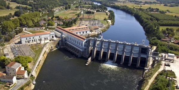 Barrage et centrale hydroélectrique vus du ciel, dans un paysage rural verdoyant.