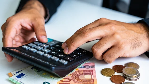 Premier plan d'une calculatrice avec des billets de banque et des pièces à côté, éclairage tamisé, composition serrée, ambiance économique froide