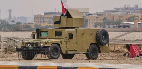 Véhicule militaire irakien Humvee avec drapeau national stationné près de barrières en béton.