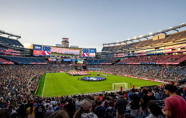 Stade bondé lors d'une cérémonie d'avant-match avec un immense drapeau américain sur le terrain.