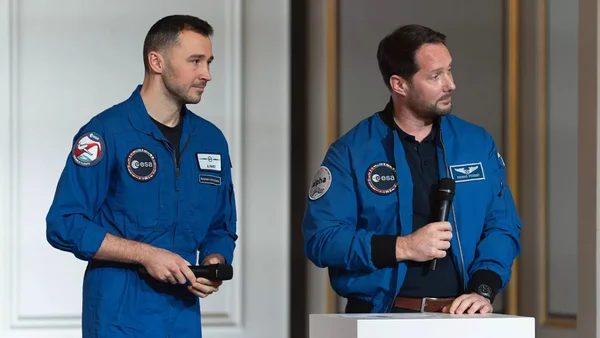 Deux astronautes français en combinaison de vol sur scène, l'un au micro.