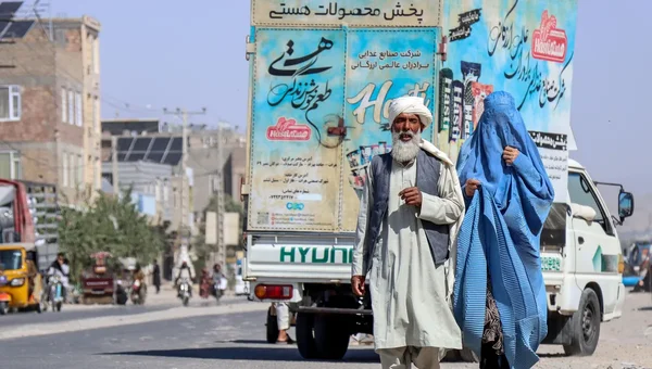 Homme âgé et femme en burqa marchant dans une rue afghane.
