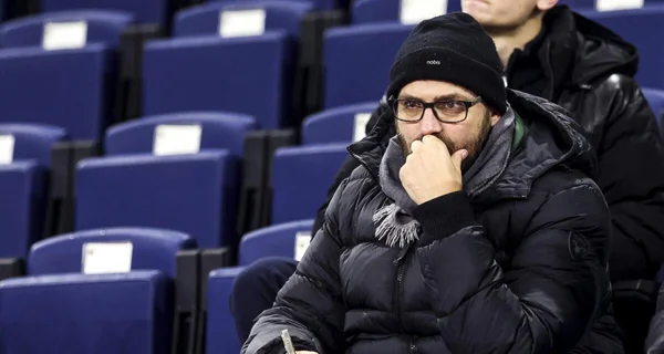 Mathieu Bodmer en bonnet et veste matelassée, assis dans un stade, en pleine réflexion.