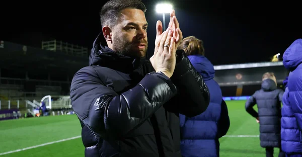 Un membre du staff de Tottenham Hotspur applaudissant sur le terrain sous les projecteurs.