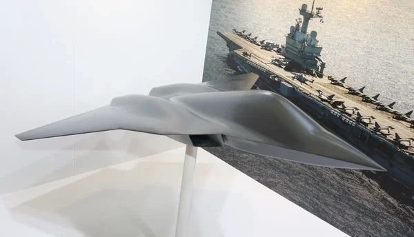 Maquette de drone furtif exposée devant un décor de porte-avions.