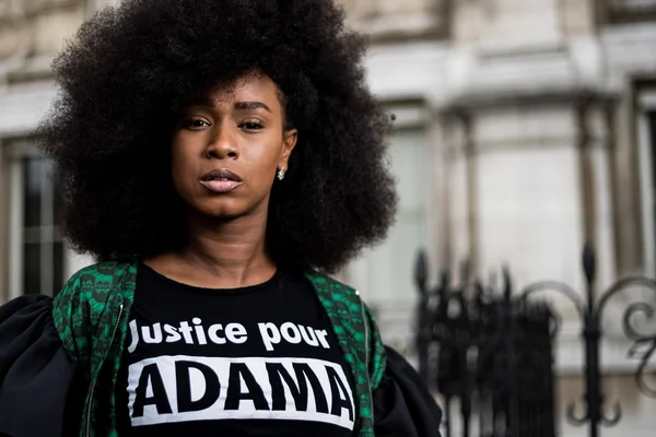 Assa Traoré en t-shirt 'Justice pour ADAMA' et veste verte, en extérieur.