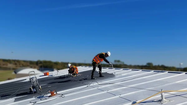 Application du revêtement réflectif Enercool sur un toit métallique par des ouvriers.