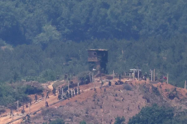 Avant-poste militaire nord-coréen sur une colline, avec une tour de guet et des soldats patrouillant à la frontière.