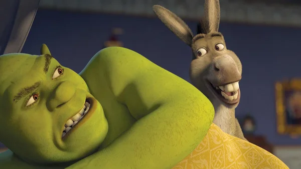 Shrek allongé dans un lit, l'Âne à ses côtés souriant.