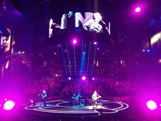 Muse en concert à Brooklyn, sur une scène circulaire baignée de lumières violettes.