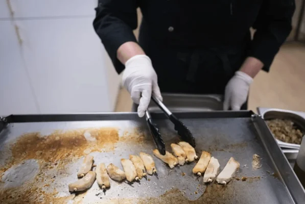 Chef cuisinant des morceaux de viande sur une plaque chauffante.