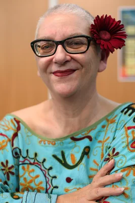 Desireless souriante, avec une fleur rouge derrière l'oreille et un haut turquoise brodé.