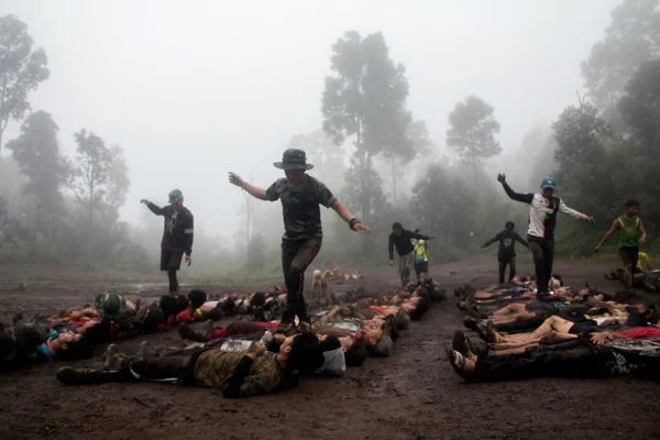 Participants à une activité en forêt brumeuse, certains allongés dans la boue, d'autres debout ou en mouvement.