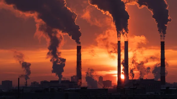Cheminées industrielles rejetant de la fumée au coucher du soleil.