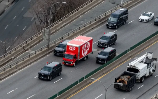 Camion KitKat rouge escorté par des SUV sur une autoroute.