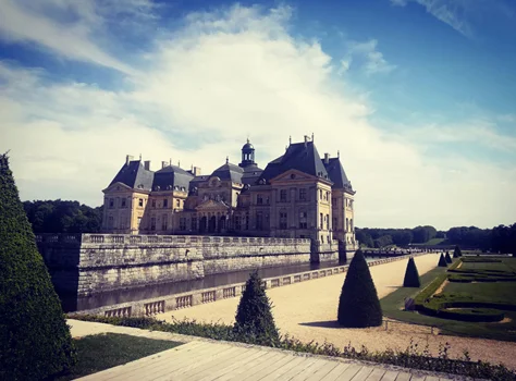 Le château de Vaux-le-Vicomte et ses jardins sous un ciel nuageux.