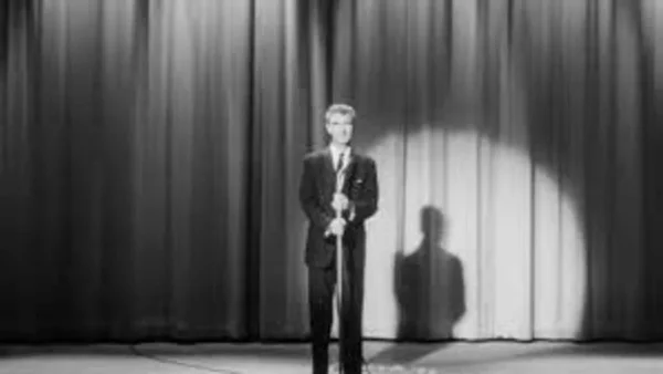Un homme en costume prononçant un discours sur scène lors d'une cérémonie d'ouverture, éclairé par un projecteur.