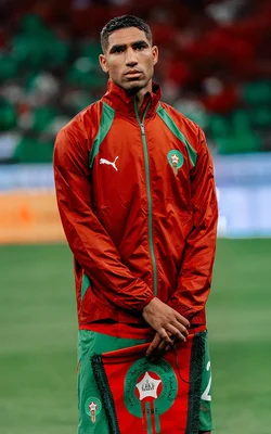 Achraf Hakimi posant avec un drapeau marocain sur un terrain de football.