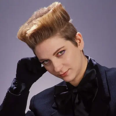 Portrait studio de Desireless dans une tenue sophistiquée avec nœud papillon et gants.
