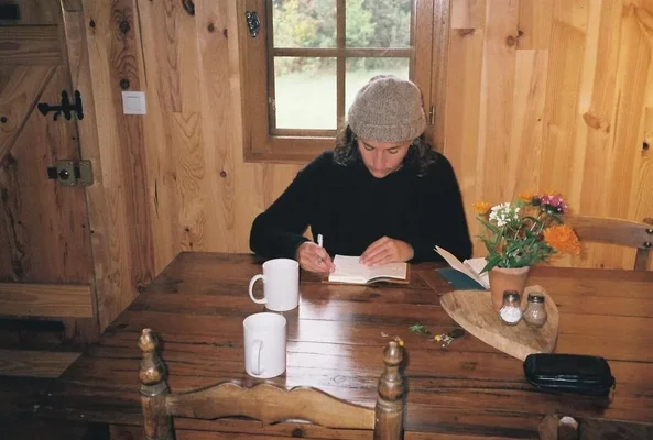 Elisa Routa écrivant dans un carnet, installée dans une cabane.