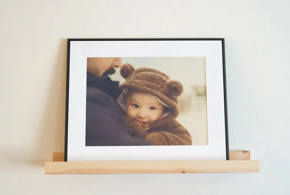 Un cadre Aura Ink affiche une photo d'un bébé avec un bonnet à oreilles d'ours, tenu par un adulte.