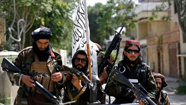 Combattants talibans en tenue militaire avec un drapeau blanc en extérieur.
