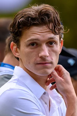 Tom Holland en gros plan, regard direct et main au menton.
