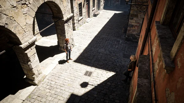 Vue en plongée d'une place de ville médiévale avec des ruelles étroites ombragées, des façades en pierre, des passants à l'ombre, forte lumière solaire contrastant avec les zones d'ombre