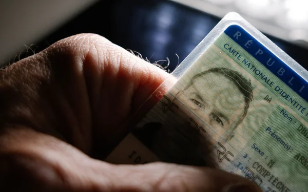 Carte nationale d'identité française tenue à la main, avec le visage du titulaire visible par transparence.