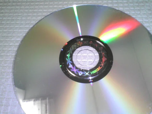 Disque de jeu Xbox original (exemple : Halo) vu de près, avec des reflets arc-en-ciel et un hologramme au centre.