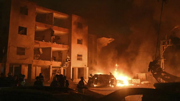 Immeuble endommagé par une frappe en Iran, avec un incendie actif et des personnes observant les dégâts.
