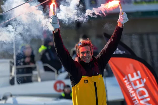 Charlie Dalin célébrant sa victoire avec des fusées éclairantes, entouré de bateaux et de spectateurs.