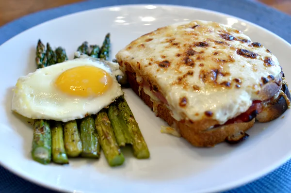Un croque-monsieur accompagné d'asperges à la milanaise et d'un œuf au plat.