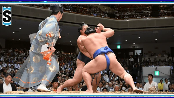 Combat de sumo professionnel : deux lutteurs s'agrippent tandis que l'arbitre en tenue traditionnelle supervise.