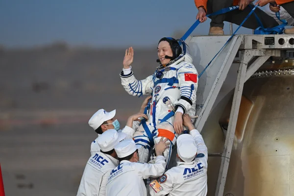 Un astronaute de Shenzhou-21 salue après être sorti de la capsule, assisté par l'équipe de récupération.