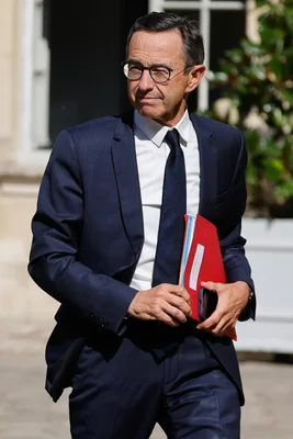 Bruno Retailleau marchant à l'extérieur, tenant un dossier rouge et un smartphone.