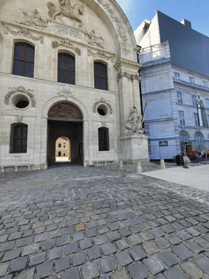 Façade de l'Hôtel des Invalides à Paris, avec sa porte voûtée et ses sculptures classiques, vue depuis la cour pavée.