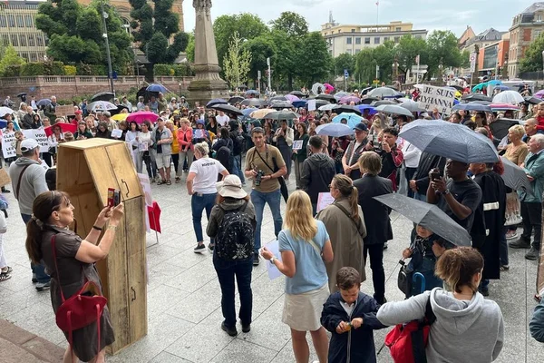 Rassemblement pour Lyhanna sous la pluie, avec un cercueil en bois au premier plan.