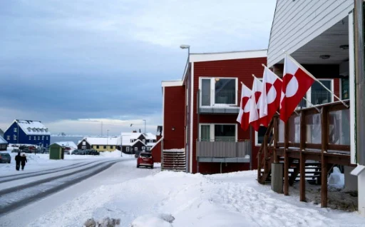 Scène de rue hivernale à Nuuk, avec un bâtiment rouge décoré de drapeaux danois et groenlandais.
