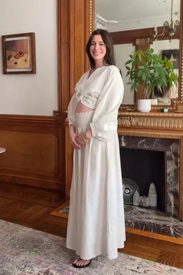 Anne Hathaway enceinte pose en tenue blanche deux pièces devant une cheminée, dévoilant son baby bump.