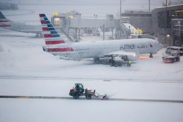 Un avion d'American Airlines sur un tarmac enneigé pendant une tempête de neige, avec des opérations hivernales en cours.