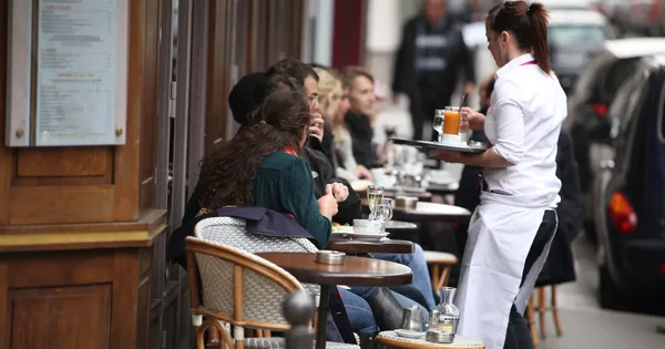 Une serveuse en terrasse sert des clients dans un café, symbole du secteur de l'hôtellerie-restauration touché par la canicule.