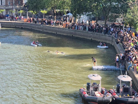 Compétition de nage en eau libre sur la Seine, suivie par de nombreux spectateurs.