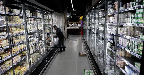 Employé approvisionnant les rayons réfrigérés d'un supermarché.